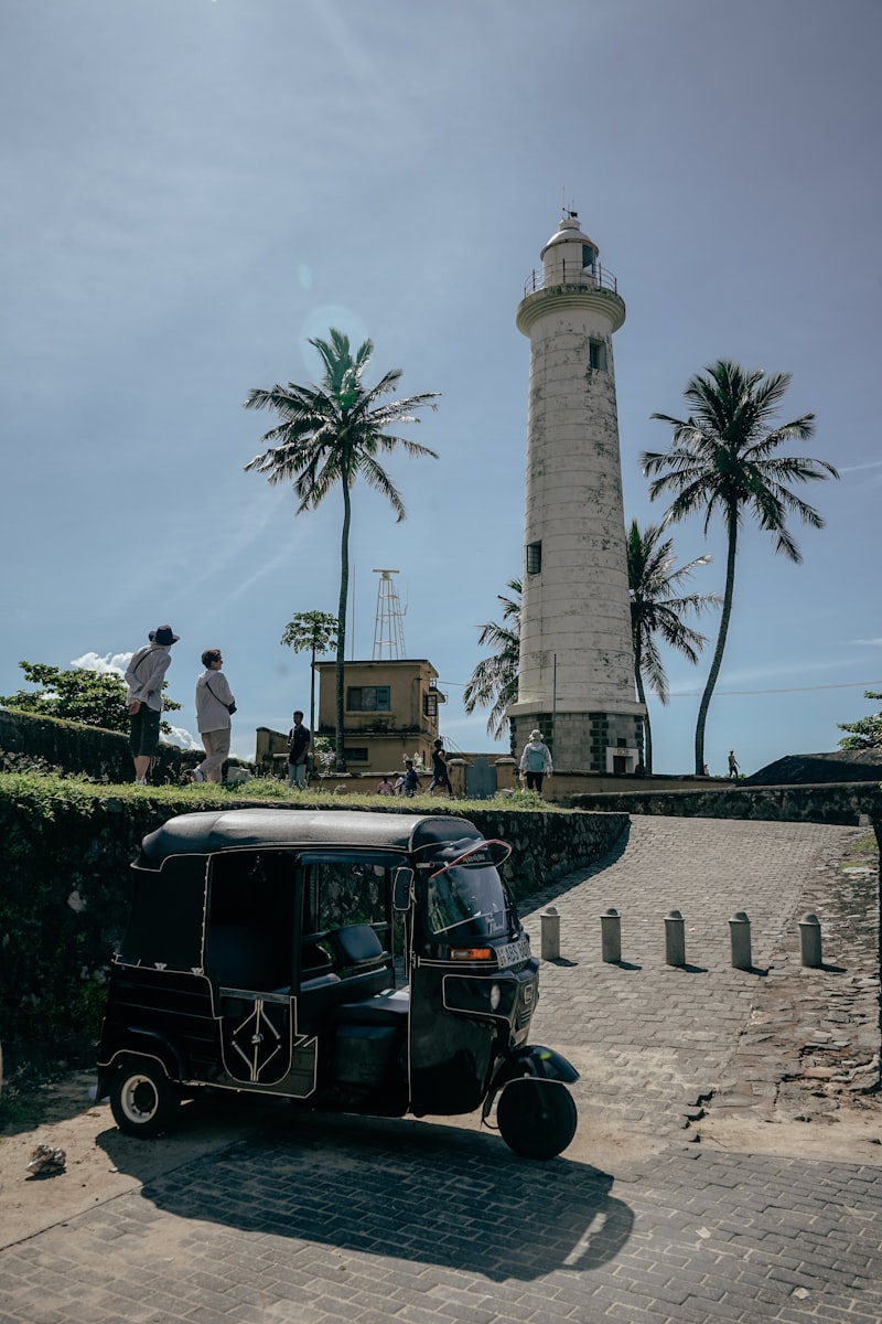 Black tuk-tuk parked near Galle Fort lighthouse with palm trees